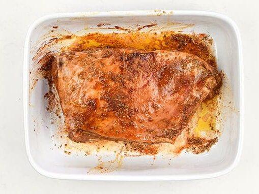 marinated lamb shoulder in a white ceramic roasting pan