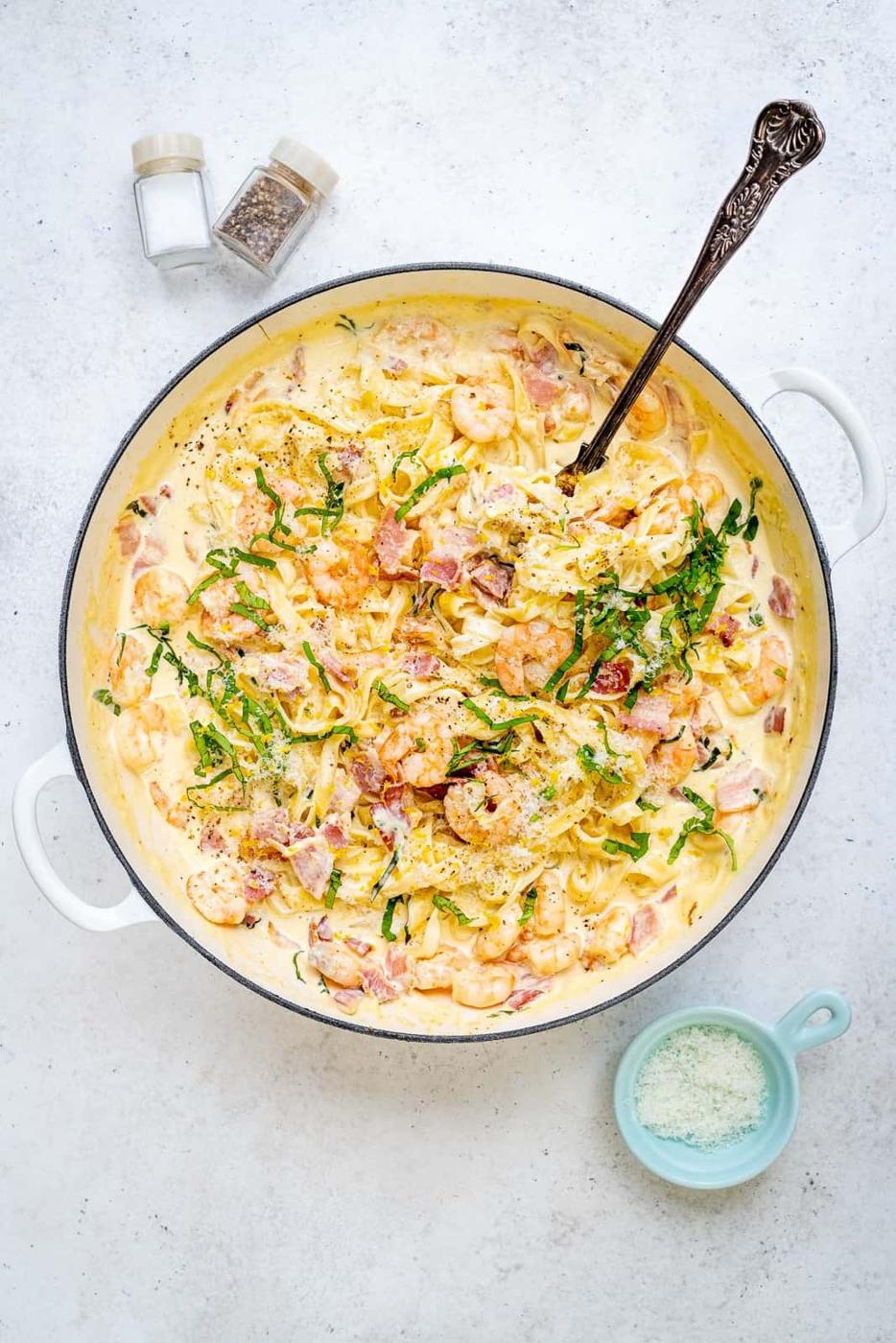 shallow casserole with creamy shrimp pasta garnished with sliced fresh basil