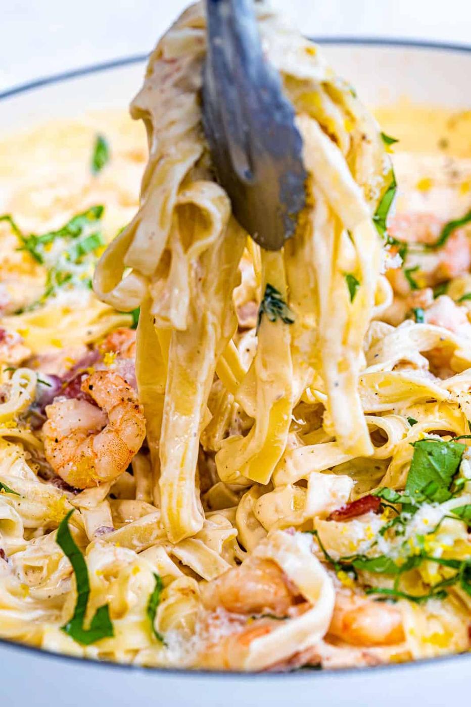 tongs picking up strands of creamy pasta
