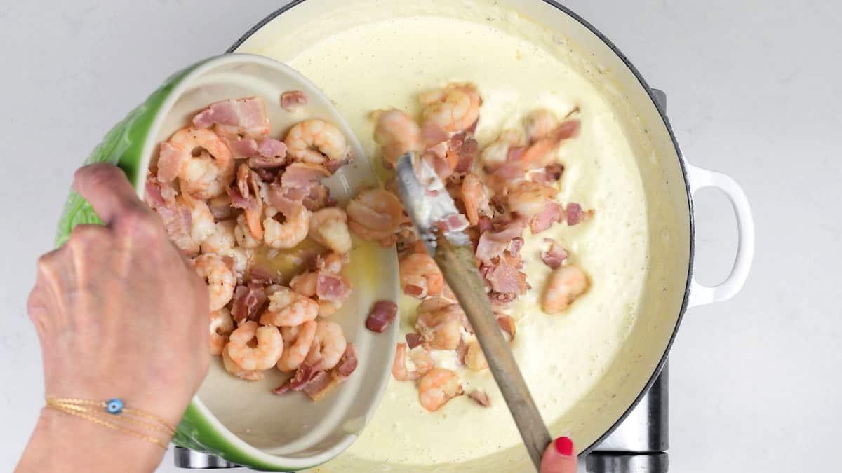 adding shrimp and bacon to creamy sauce