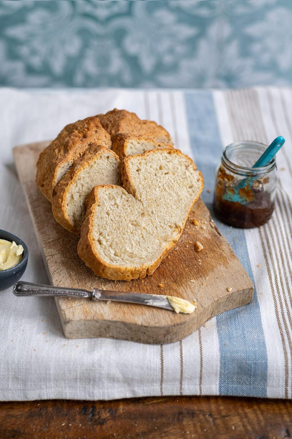 slices of soda bread on a cutting board, butter knife and pot of jam on the side