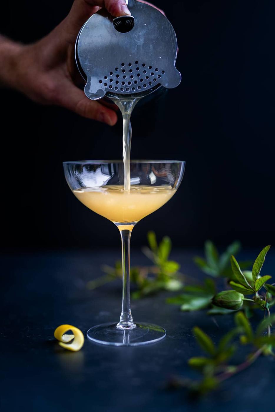 straining an absinthe cocktail into a coupe glass