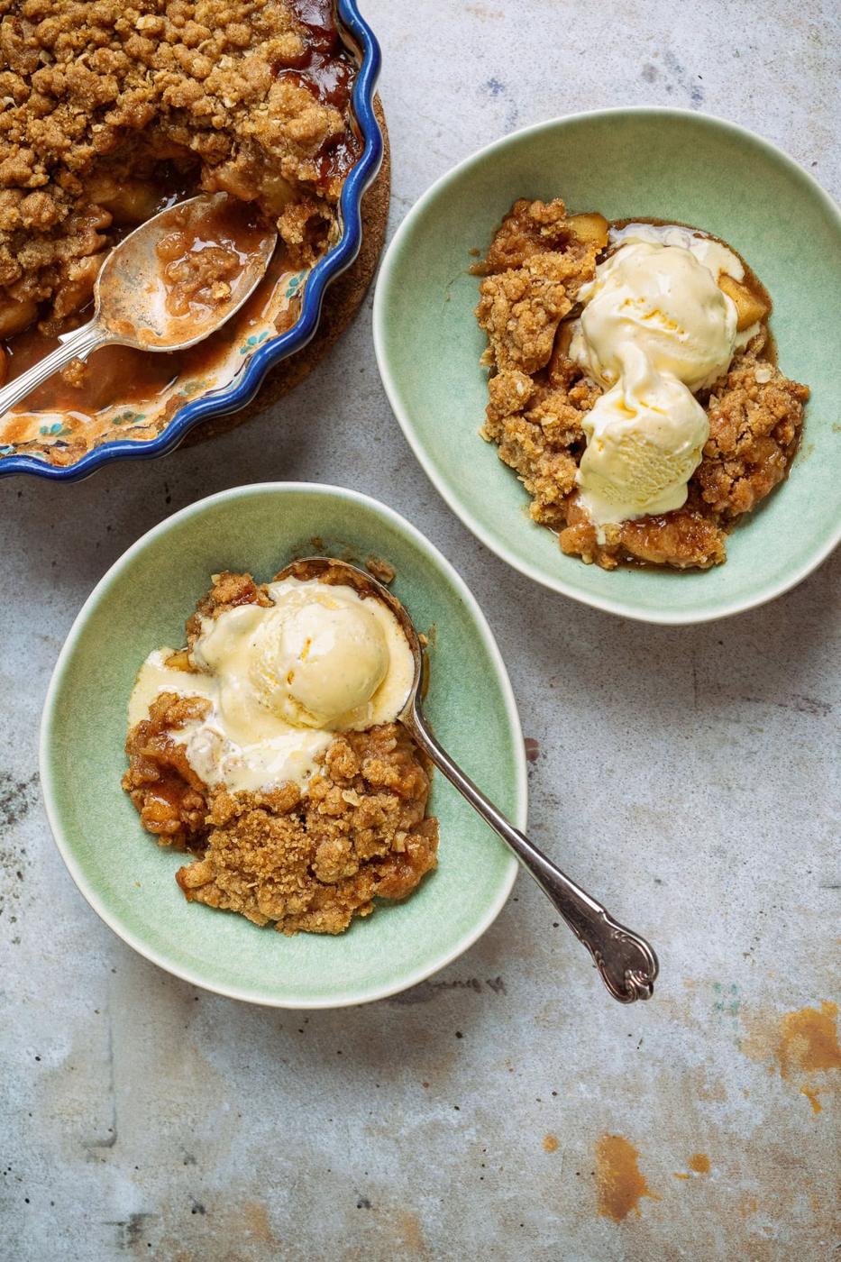 two bowl servings of apple crumble with vanilla ice cream, pie dish on the side