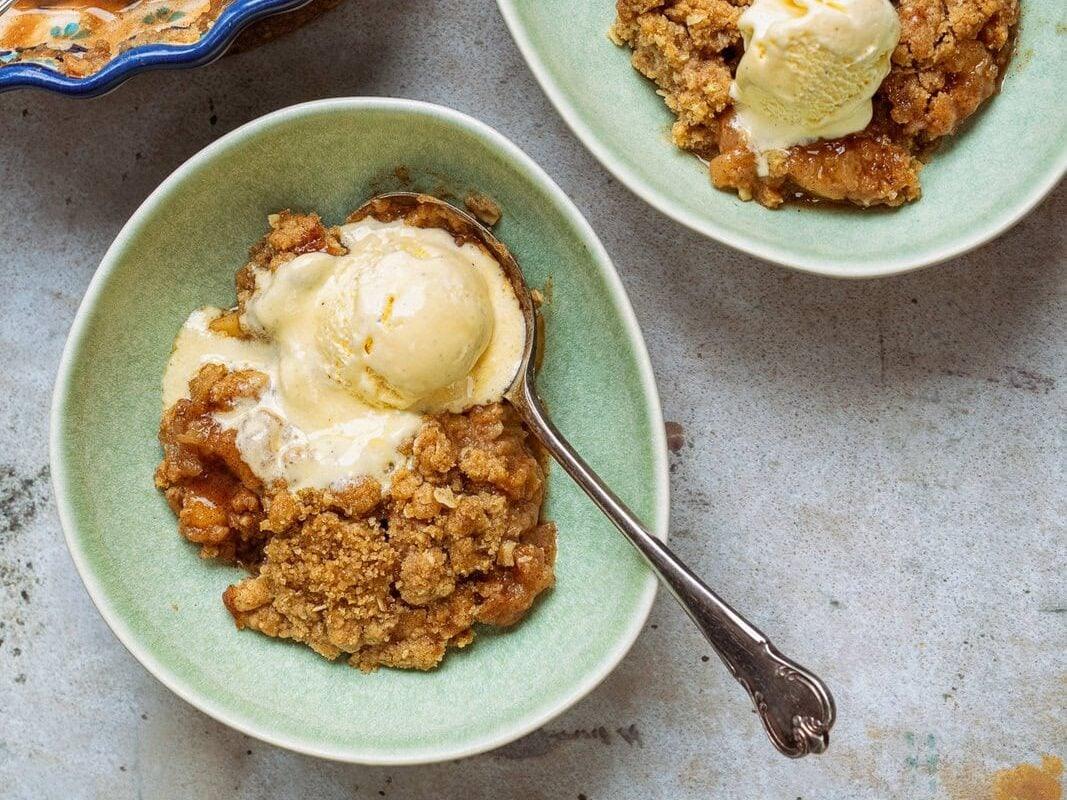 two bowl servings of apple crumble with vanilla ice cream, pie dish on the side