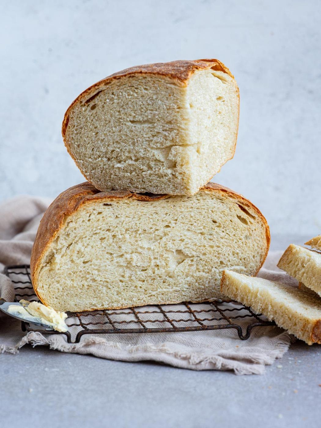 A stack of two freshly sliced halves of a round loaf of air fryer bread on a wire cooling rack, with a butter knife beside it.