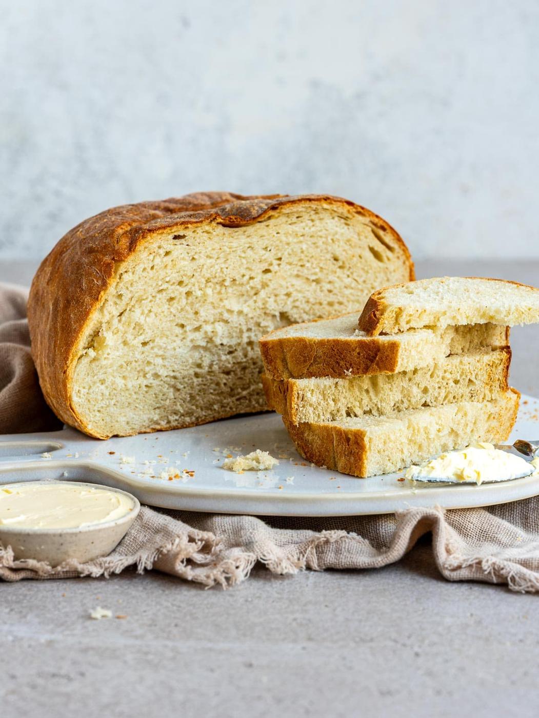 A loaf of sliced air fryer bread on a serving platter with a small dish of butter and a butter knife.