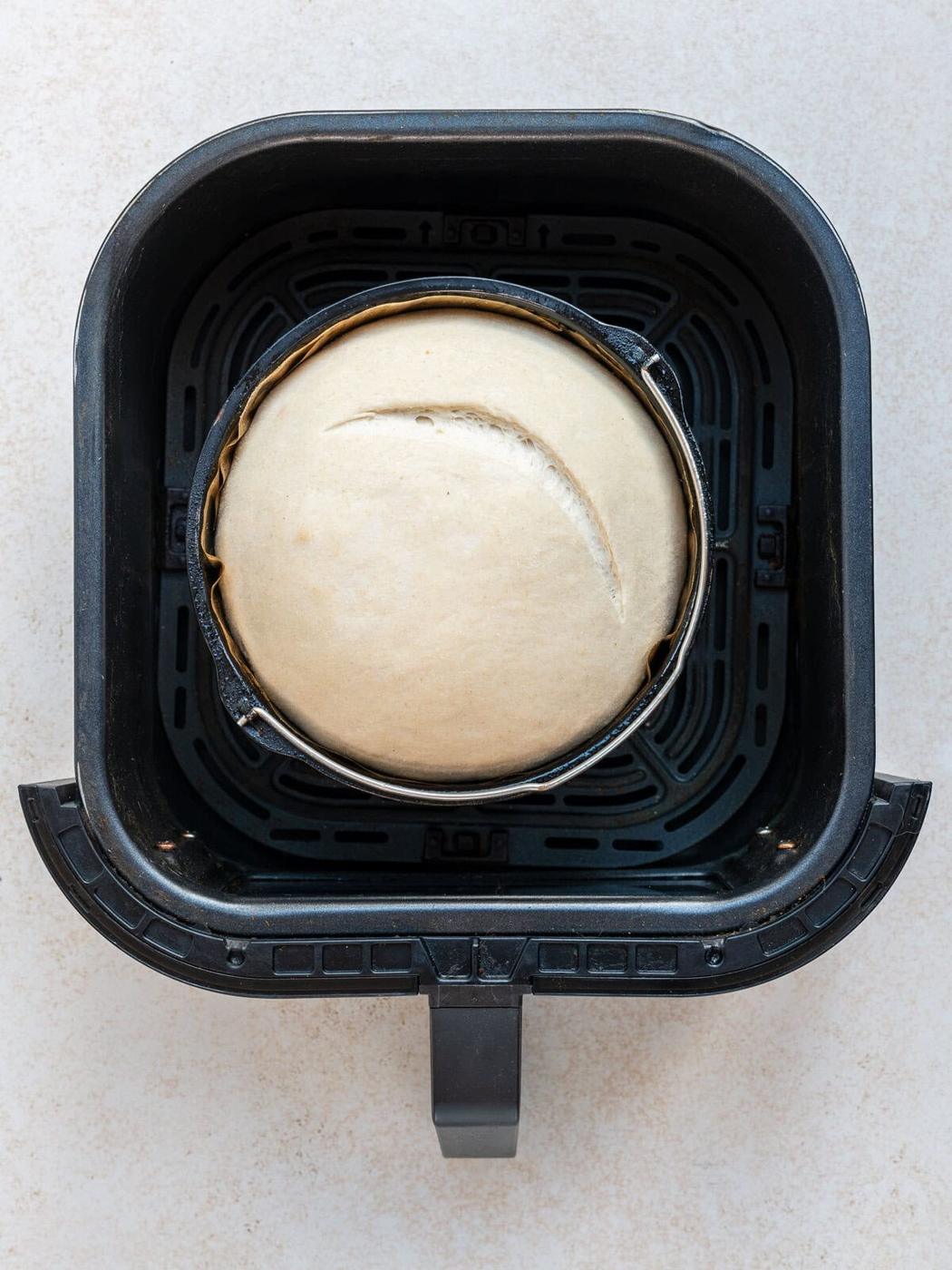 Unbaked bread in an air fryer basket, shaped as a loaf inside a round pan.