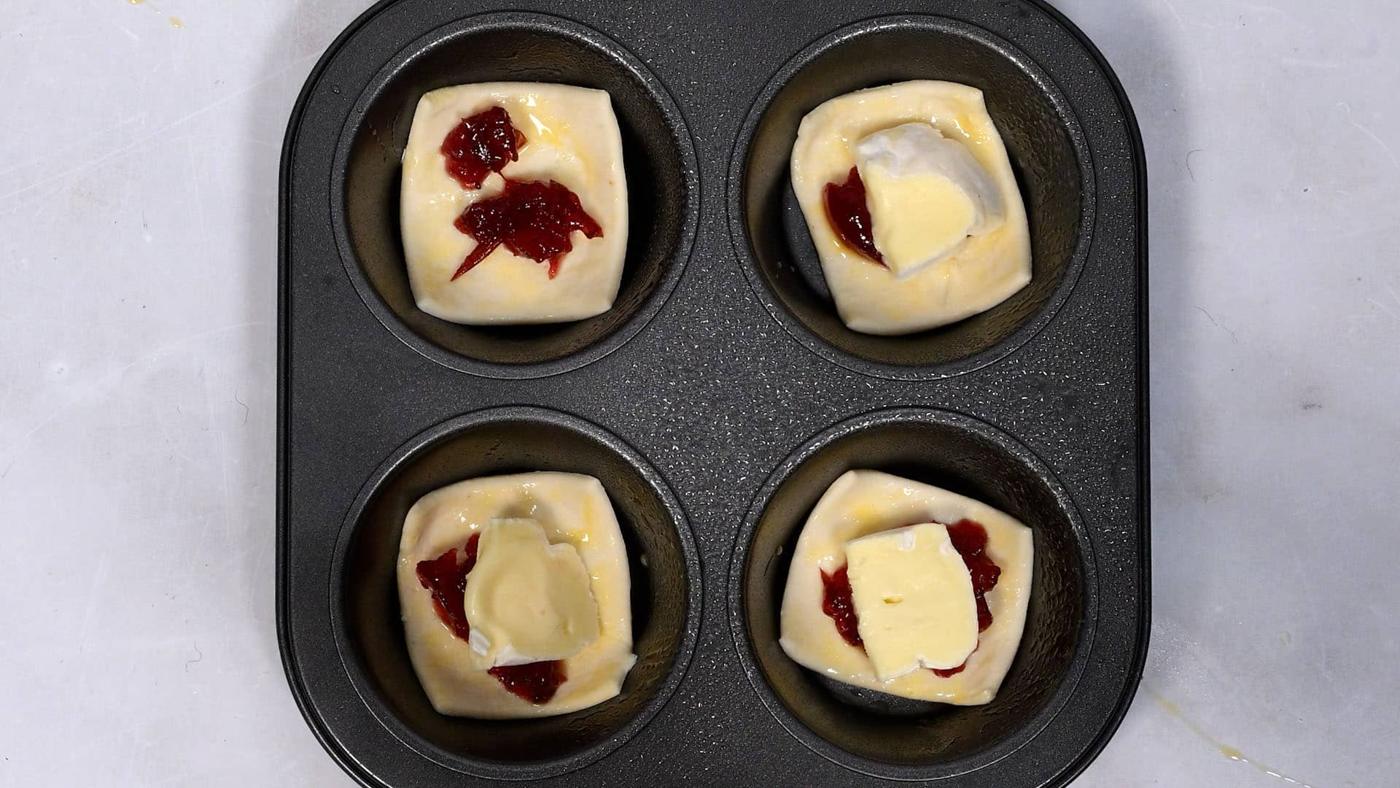 muffin tray with puff pastry topped with cranberry sauce and cubes of brie