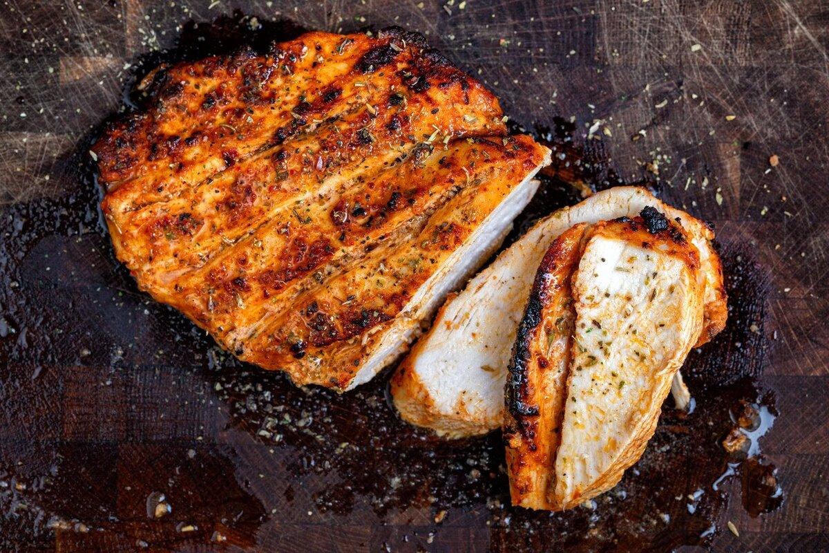 air fried, seasoned chicken breast sliced on a dark wooden cutting board, showing juicy, well-cooked meat and a golden-brown, slightly charred exterior.