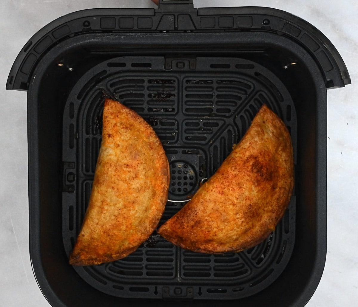 two chicken crispanadas in the basket of an air fryer