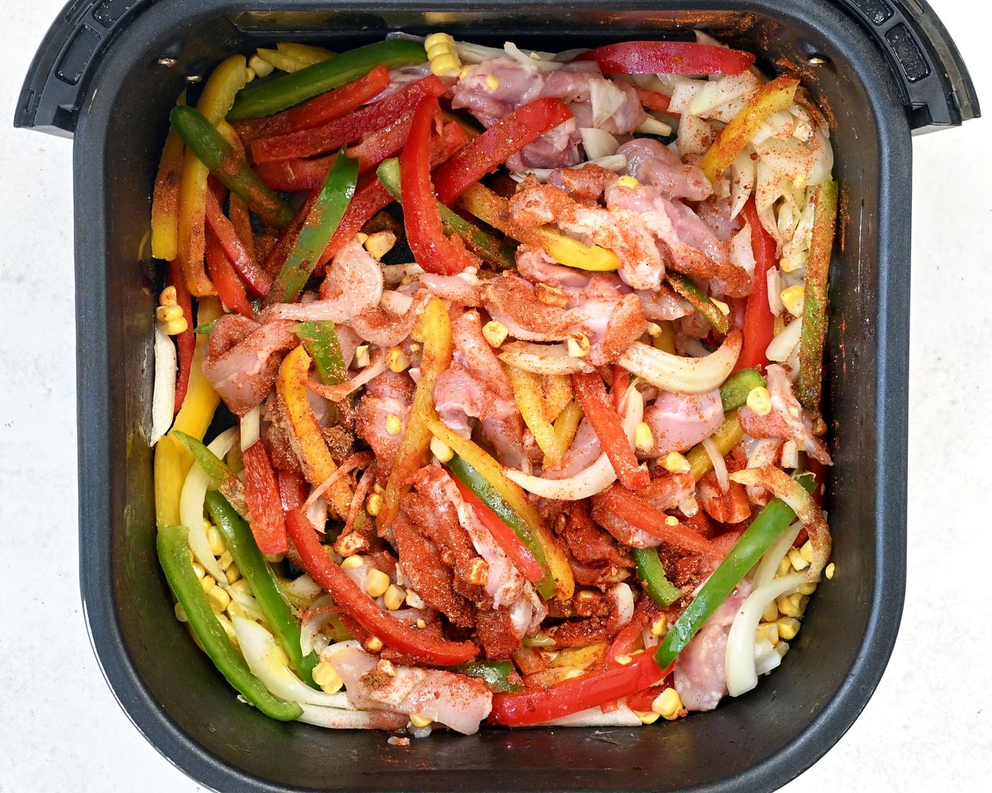 chicken strips, peppers, onion and seasoning in the basket of an air fryer