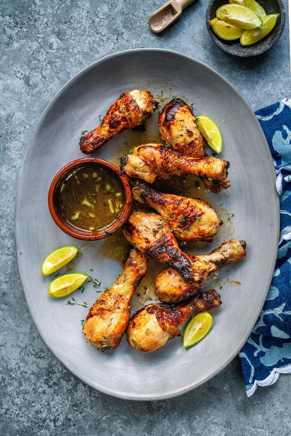 platter with golden juicy chicken drumsticks, lime wedges and dipping sauce