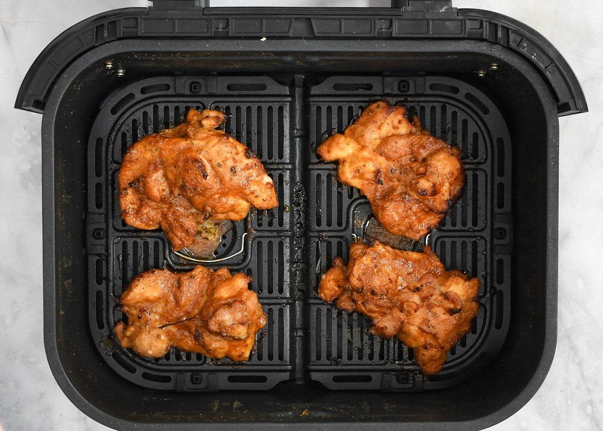 marinated chicken thighs in the basket of an air fryer