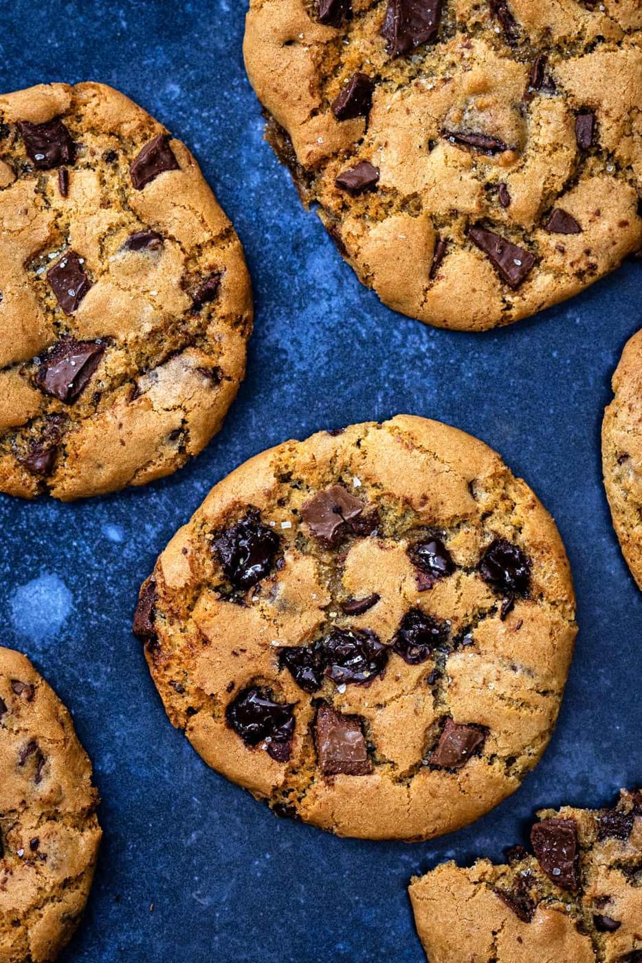 Chocolate chip cookies with chunks of chocolate are arranged on a dark blue surface. These golden brown treats look deliciously homemade—perfect examples of how easy and tasty air fryer cookies can be.