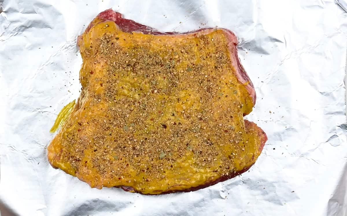 Corned beef brisket covered with mustard and honey paste on a piece of foil