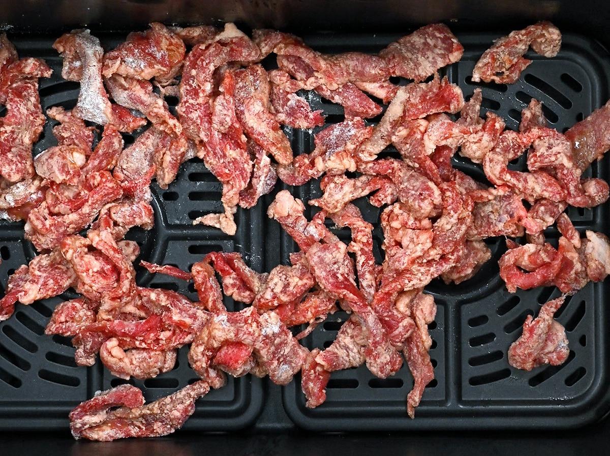 close up on beef strips coated in cornflour in the basket of an air fryer