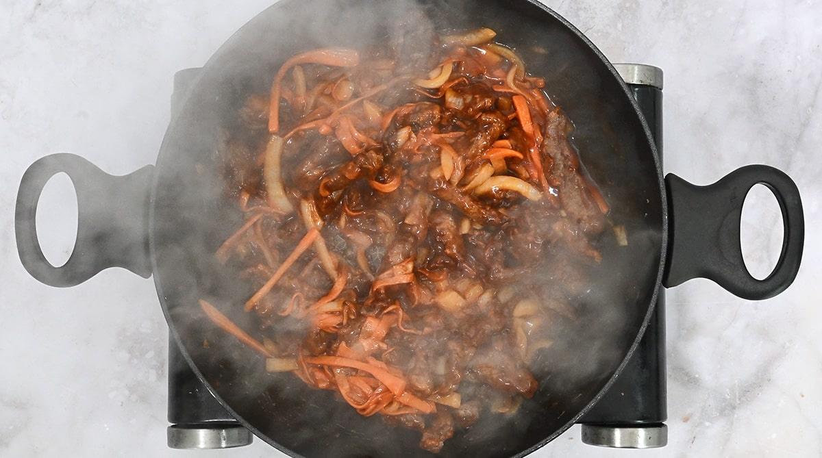 Coating crisp beef strips in a tangy sauce in a wok