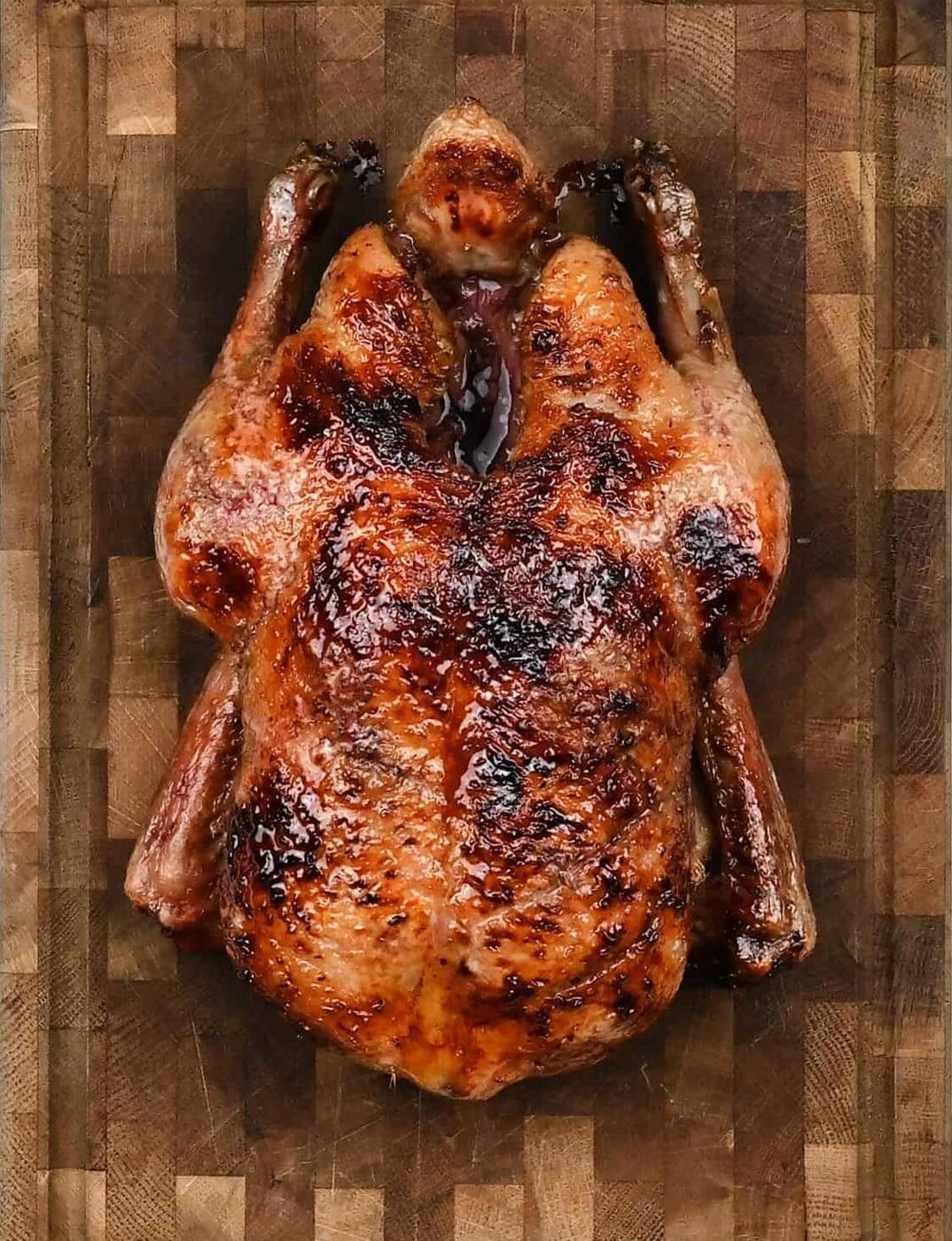 A whole Air Fryer Duck with crispy, golden-brown skin rests on a wooden cutting board, viewed from above.