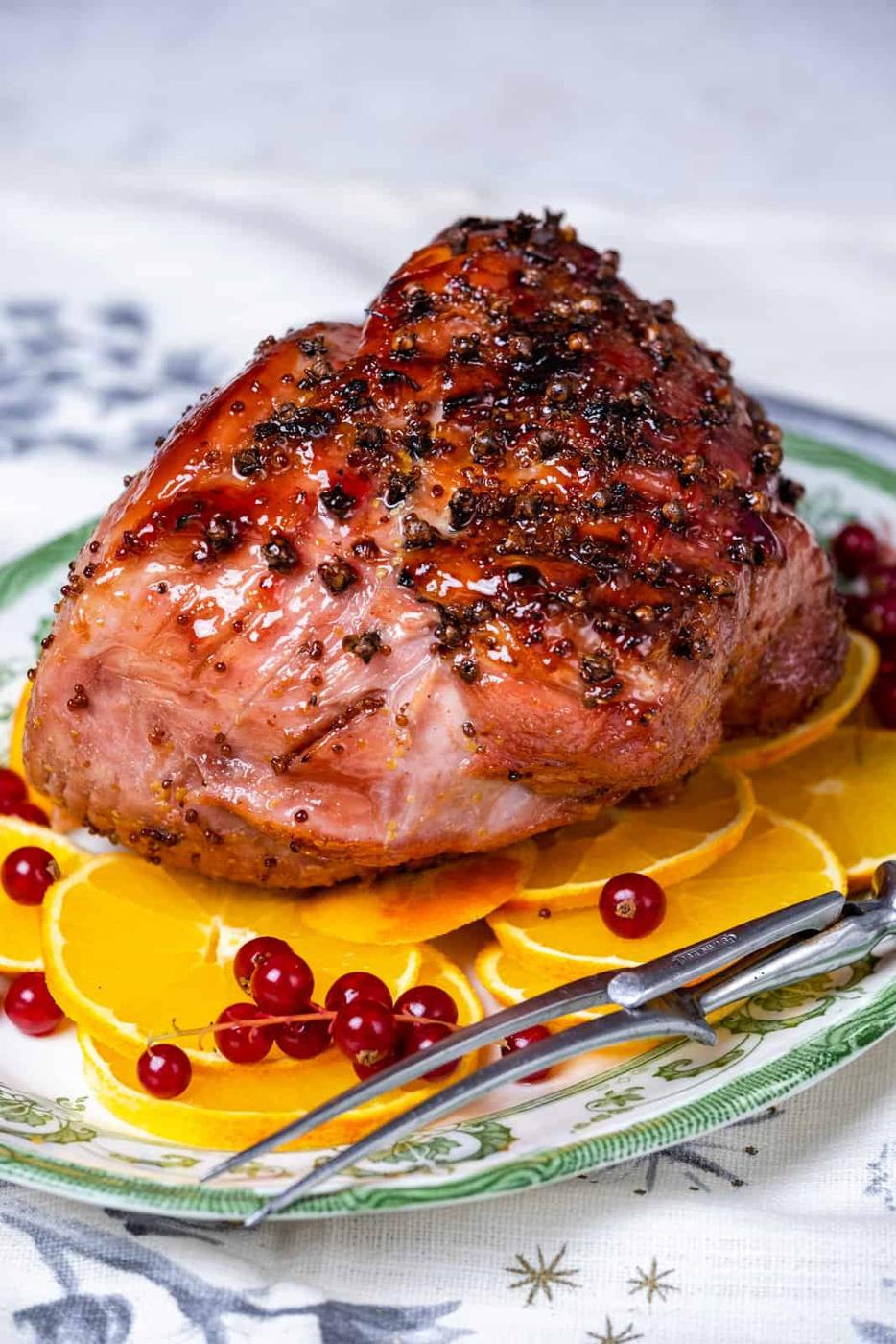 Glazed ham cooked in an air fryer on a platter with orange slices and cranberries