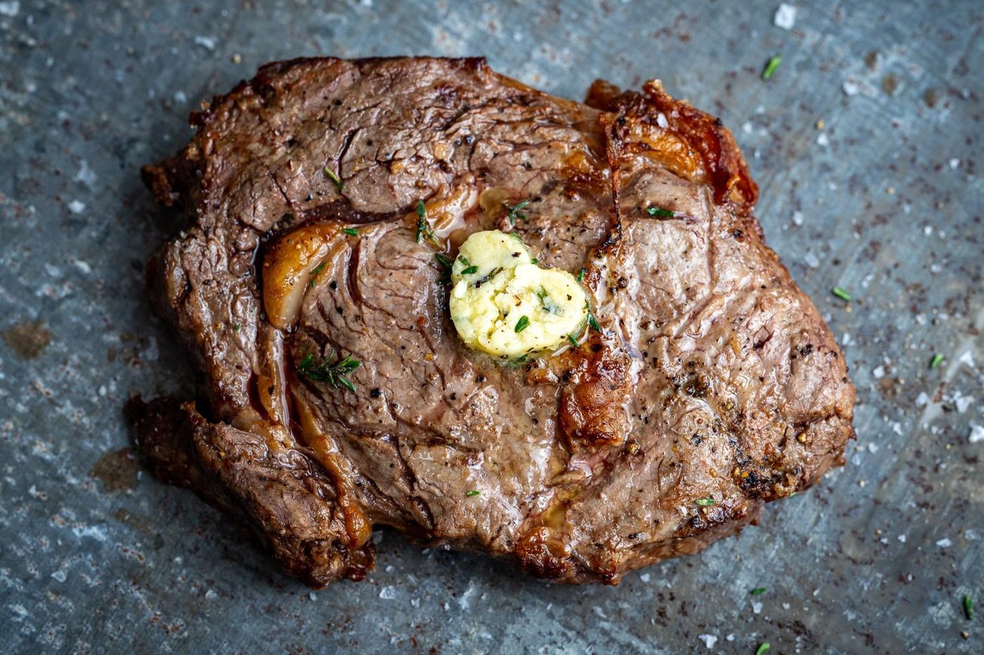 Air fryer rib eye steak on a zinc surface, topped with a pat of garlic butter