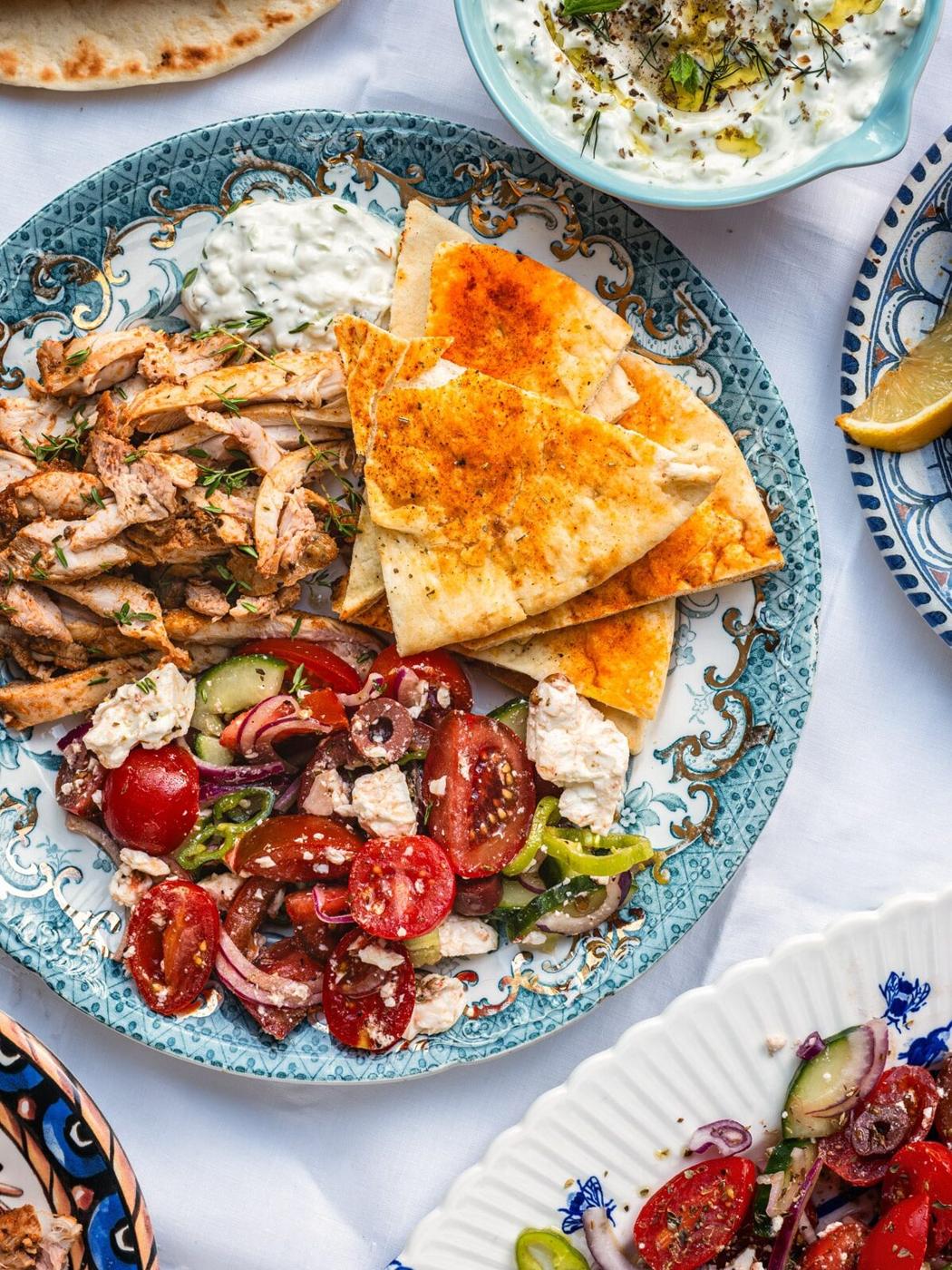 Air Fryer Greek chicken served sliced with Greek salad, pita bread and tzatziki on a patterned plate