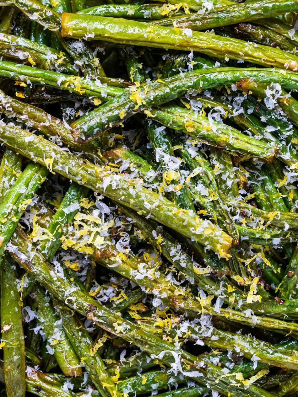 A close-up of air fryer green beans topped with grated Parmesan cheese and lemon zest, showing vibrant green colors and a sprinkling of seasoning.