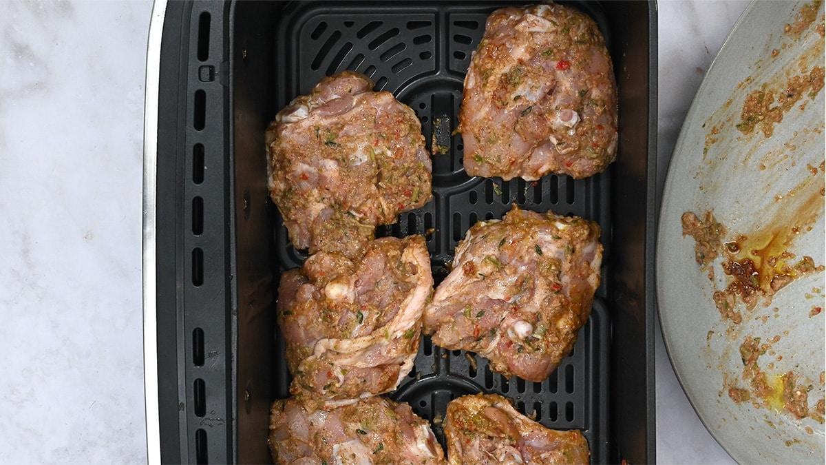 marinated chicken thighs in the basket of an air fryer