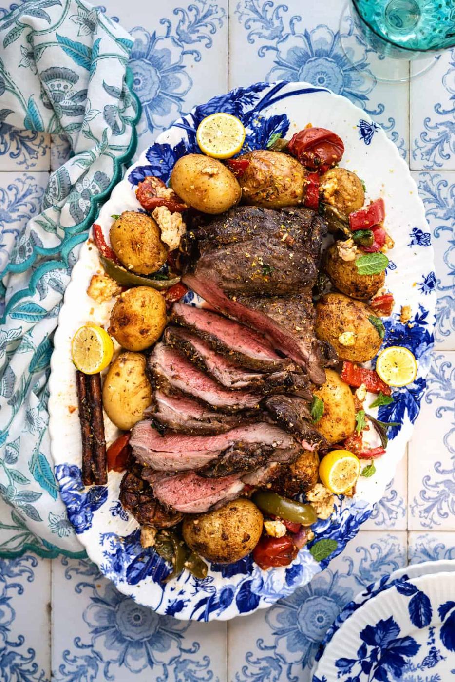 Lamb kleftiko served on a platter with potatoes, peppers, tomatoes and feta