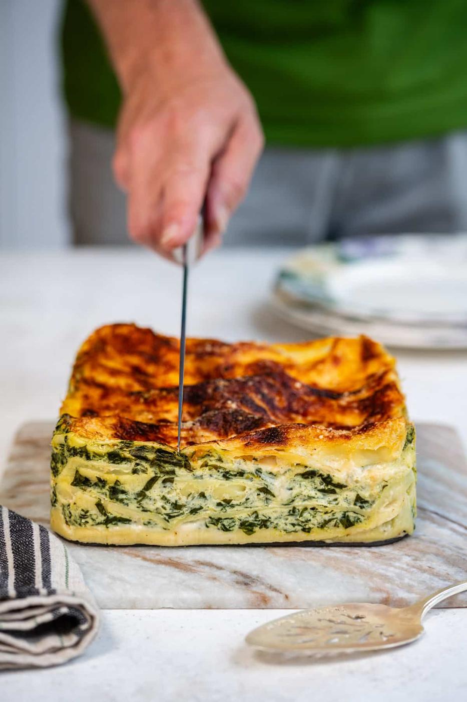 Hand slicing Air Fryer lasagna on a marble board
