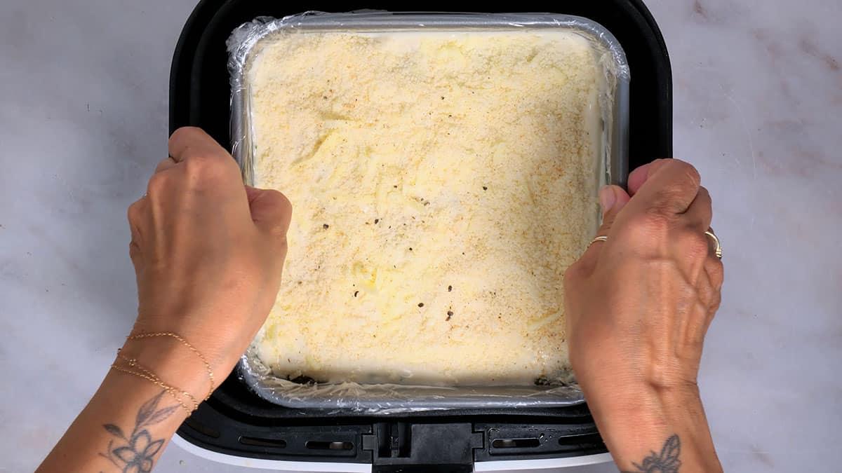 putting a pan of lasagna in an air fryer basket