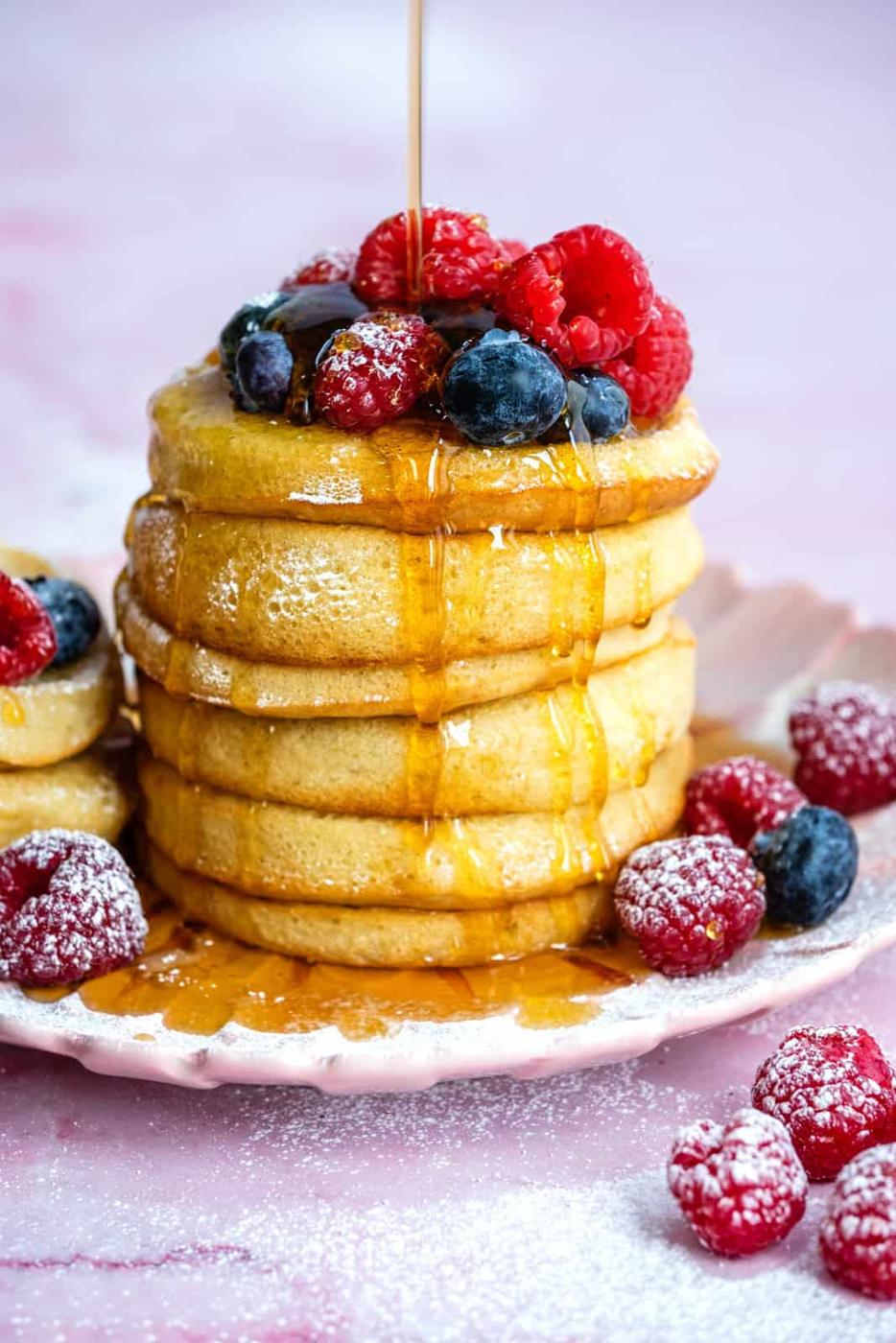 Stack of air fryer pancakes on a plate topped with blueberries and raspberries and drizzled with syrup