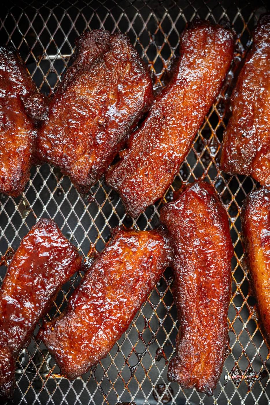 Barbecue pork strips with a glossy, caramelized glaze are arranged on a metal grill grate, their rich reddish-brown color indicating they are freshly cooked and ready to eat.