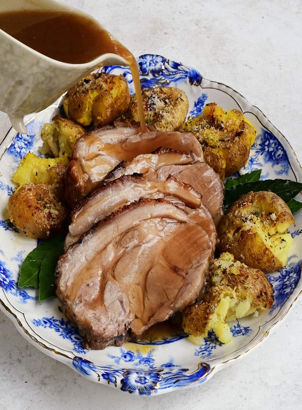 Pouring gravy over roast pork slices on a platter