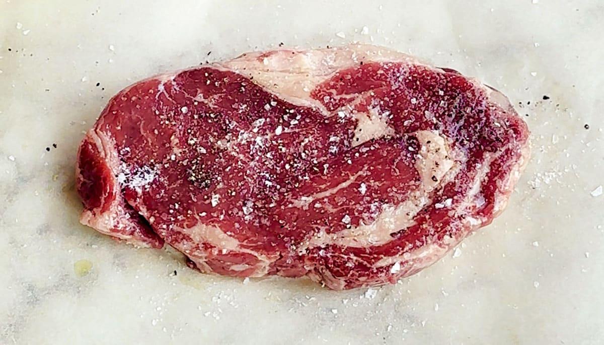 raw thick cut ribeye steak seasoned with salt and pepper
