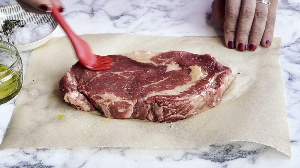 brushing a raw steak with olive oil
