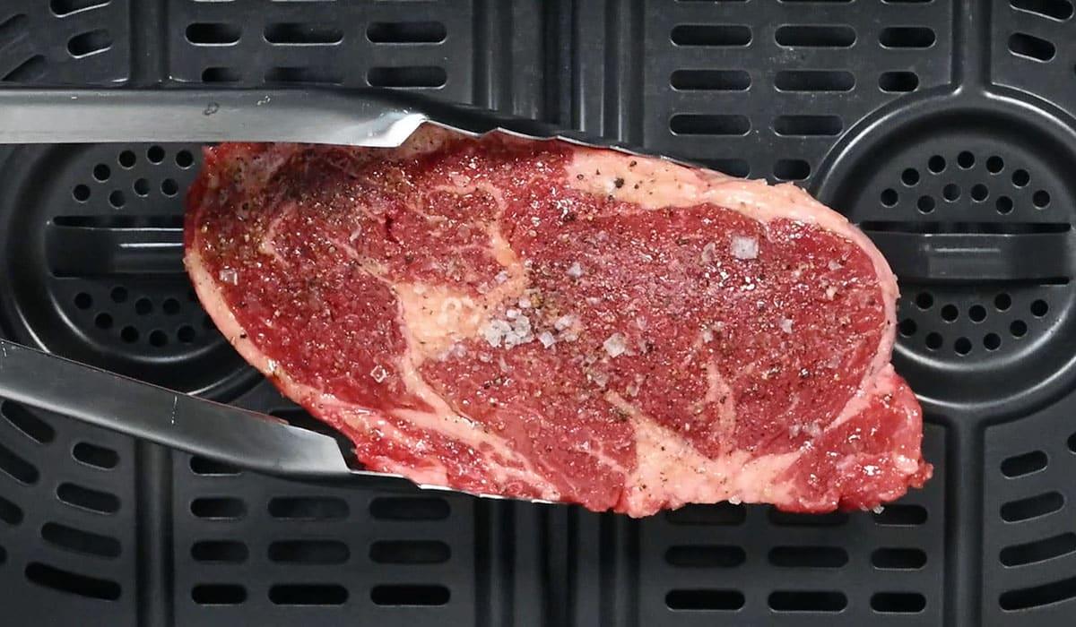 adding a ribeye steak into the basket of an air fryer