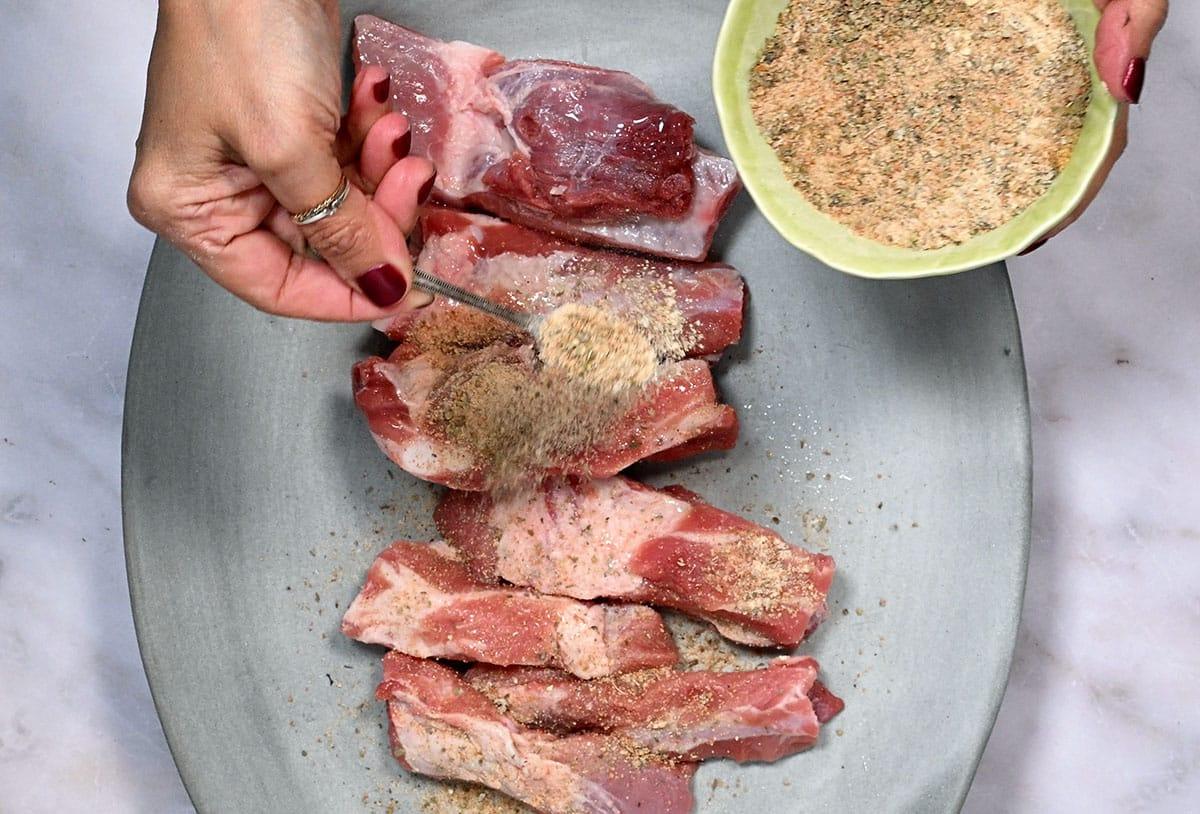 adding dry rub over pork ribs in a platter