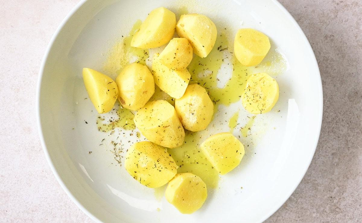 potatoes in a white bowl with olive oil and seasoning