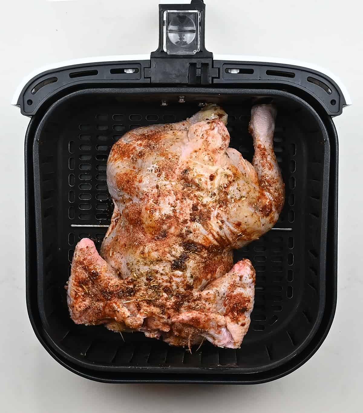 Whole seasoned chicken placed breast side down in an air fryer basket