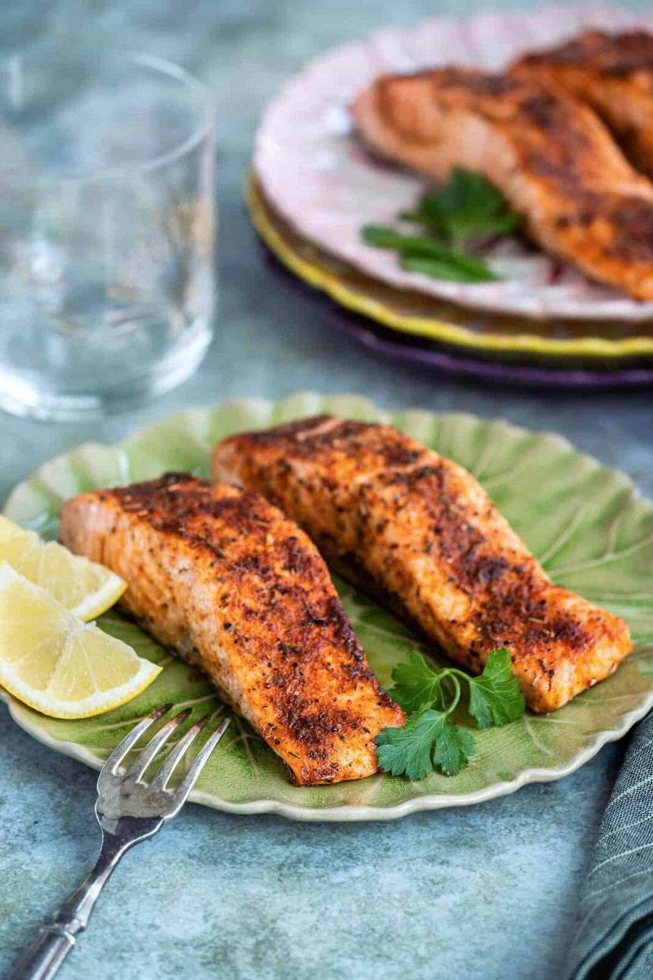 Two salmon fillets served on a green plate with lemon on the side