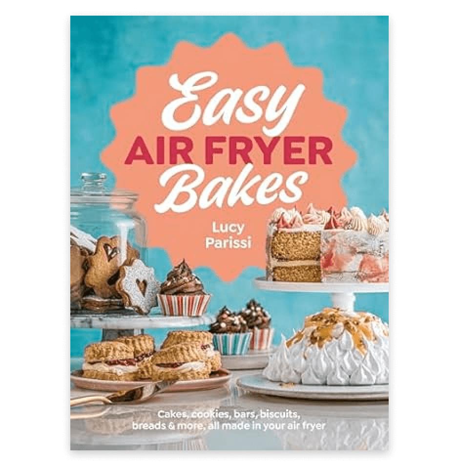 The cover of the book Easy Air Fryer Bakes by Lucy Parissi, creator of Nusde, features cakes, cookies, cupcakes, and desserts on cake stands and plates against a blue and orange background.
