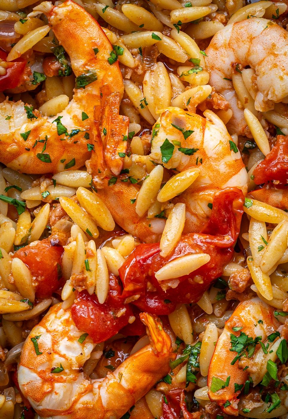 Close-up of cooked orzo pasta mixed with shrimp, chorizo, and cherry tomatoes, garnished with chopped parsley. The dish appears to be well-seasoned and freshly prepared.