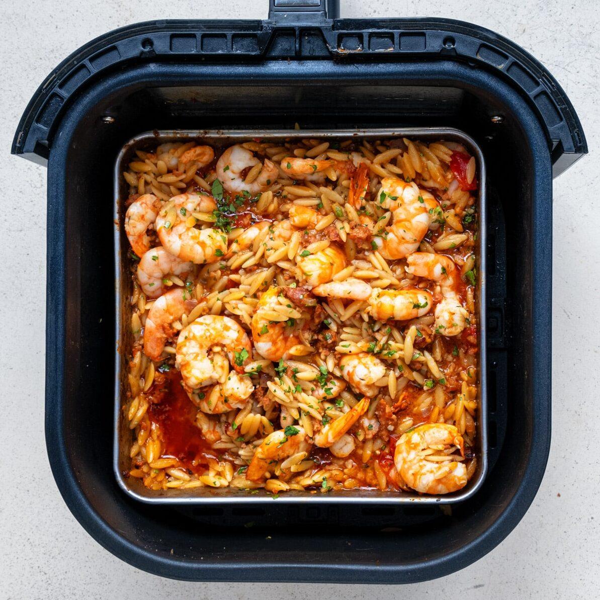 Shrimp and orzo pasta in a rich tomato sauce with cherry tomatoes, garnished with herbs and cooked inside an air fryer basket—a delicious shrimp orzo recipe for easy weeknight meals.
