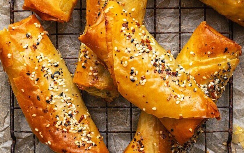 stack of crisp golden air fryer spanakopita rolls on a small wire rack against blue background
