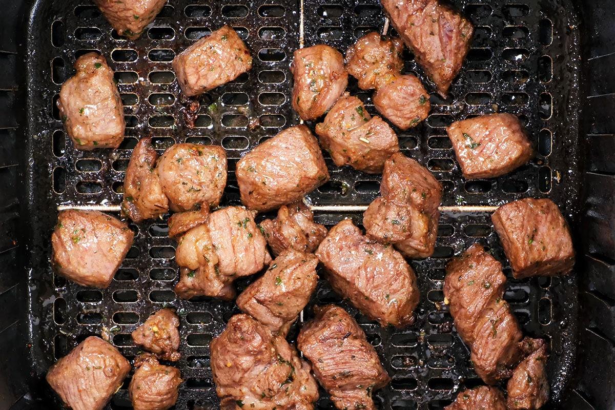 Air Fryer Steak Bites are shown as cubed pieces of cooked steak spread out in an air fryer basket, each with a browned and seasoned exterior.