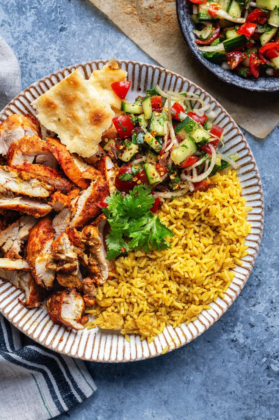 tandoori chicken thigh, sliced and served with turmeric rice, naan bread and salad