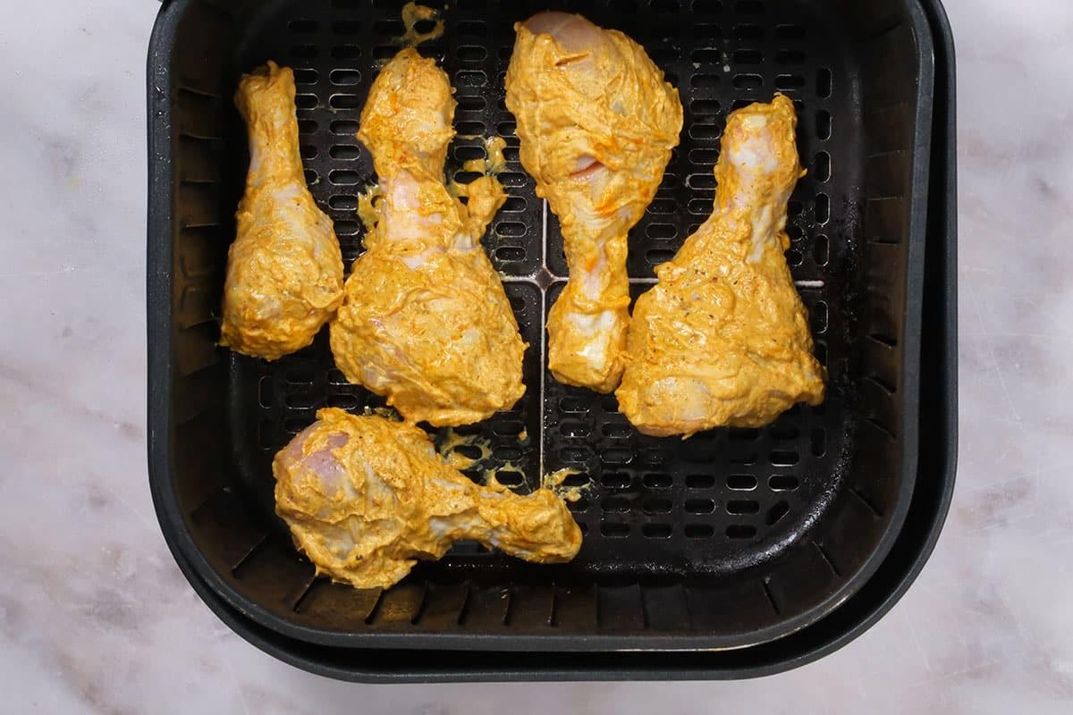 raw tandoori chicken drumsticks in an air fryer basket