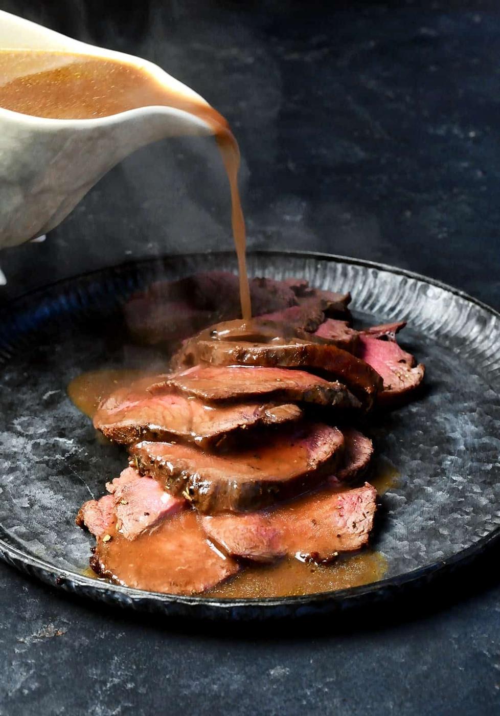 Gravy being poured over sliced roast venison