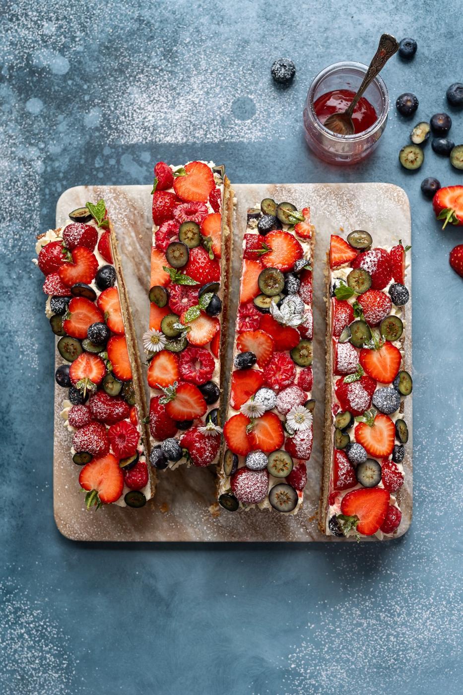 Sliced Victoria sponge cake tray bake with fresh berries and whipped cream on a marble board