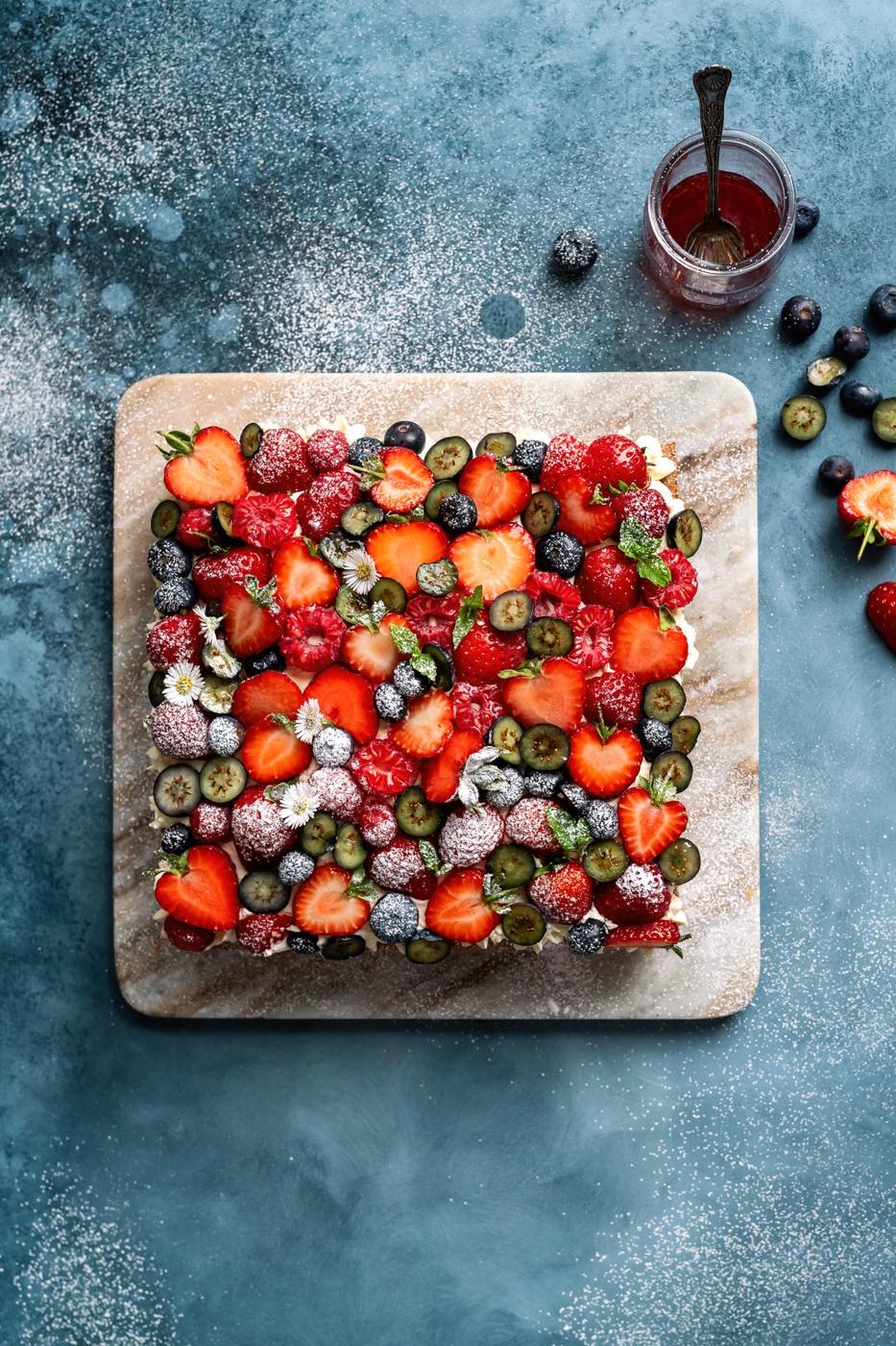Victoria Sponge tray bake decorated with a medley of fresh berries against a blue background